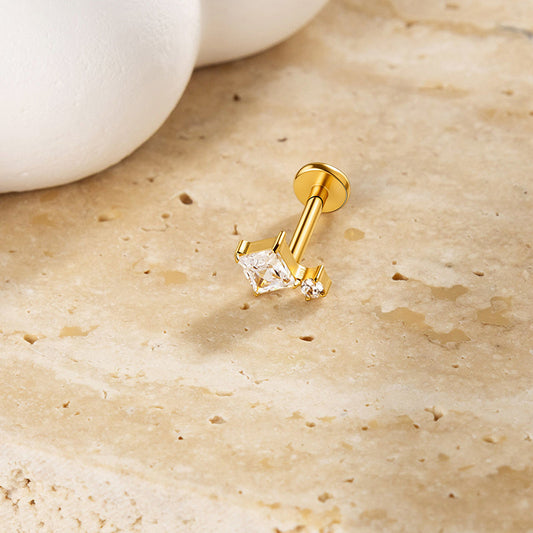 Gold-colored princess-cut CZ flat-back stud resting on a cream stone surface; catalog example of internally threaded jewelry