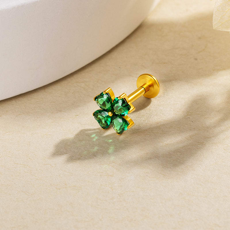 Green heart-shaped clover stud with a gold-colored setting on a beige surface.