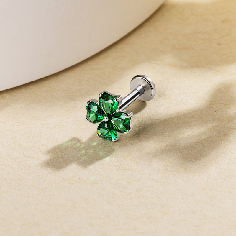 Green heart-shaped clover stud with a silver-colored setting on a beige surface.